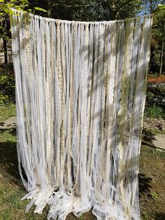 a white curtain hanging from the side of a tree in front of some grass and trees