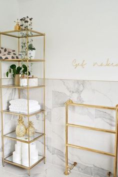 a bathroom with marble walls and gold shelving unit holding towels, toiletries and plants