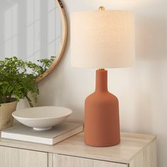 a table lamp sitting on top of a wooden dresser next to a bowl and mirror