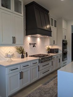 a large kitchen with white cabinets and black stove top hood over the range in front of an oven