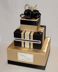 three tiered black and gold wedding cake with ribbon on top, decorated with pearls