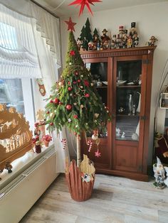 a small christmas tree in a pot on the floor next to a cabinet and window