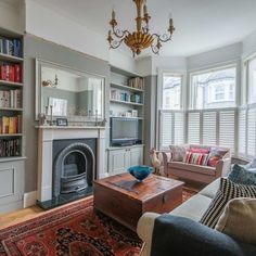 a living room filled with furniture and a fire place under a chandelier in front of a window