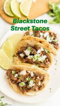 three tacos on a plate with limes and cilantro in the background