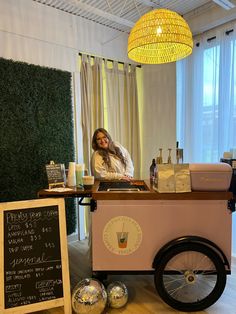 a woman standing behind a food cart with drinks on it