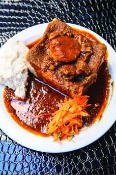 a white plate topped with meat and gravy next to mashed potatoes on a table