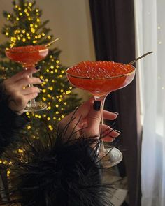 two people holding up wine glasses in front of a christmas tree with lights on it