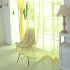 a yellow chair sitting in front of a window next to a table with a lamp on it