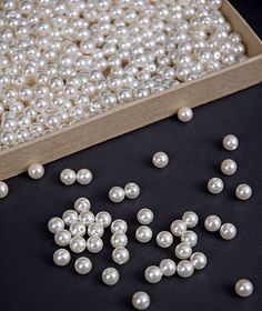 white pearls are scattered on a black surface next to a wooden box with beads in it