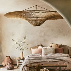 a large bed sitting under a hanging light in a bedroom next to a table with two vases on it