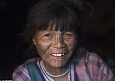 a woman with tattoos on her face and chest smiles at the camera while standing in front of a dark background