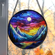 a stained glass sun catcher hanging from a window with autumn leaves in the foreground