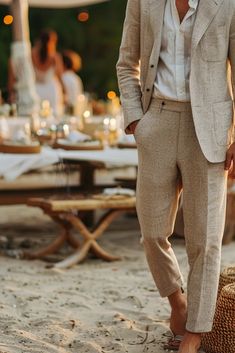 a man in a suit standing on the beach with his hands in his pockets and shoes