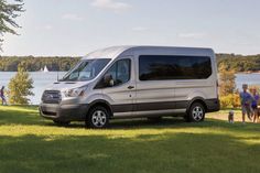 a silver van parked on top of a lush green field next to a body of water