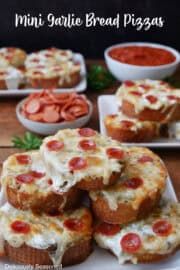 mini garlic bread pizzas with pepperoni and cheese spread on the top, sitting on white plates