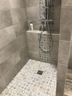 a walk in shower sitting next to a tiled wall and floor covered in grey tiles