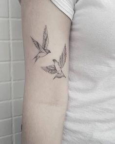 a woman's arm with two birds flying in the sky on her left side