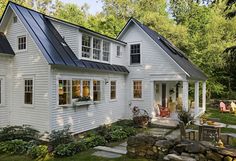 a white house with a black metal roof and some plants in the yard next to it