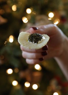 a hand holding a piece of fruit with a christmas tree in the background