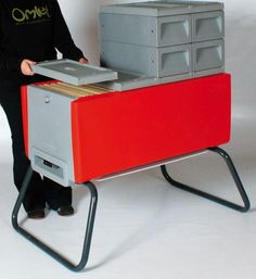 a woman standing next to a red and grey desk with drawers on it's legs