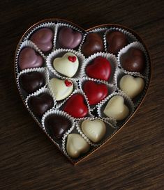 a heart shaped box filled with assorted chocolates on top of a wooden table