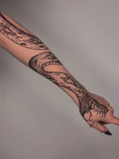 a woman's arm with a snake tattoo on it and a hand holding an object