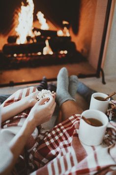 two people sitting in front of a fire with their feet up on the floor eating food