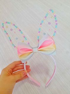 a hand is holding a pink and white bow headband with beads on it,