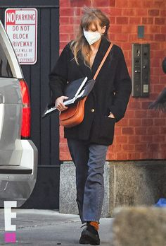 a woman walking down the street wearing a face mask and carrying a book in her hand