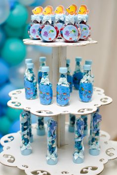 there is a three tiered cake stand with bottles on it and blue balloons in the background