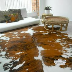 a brown and white cowhide rug on the floor in a living room next to a couch