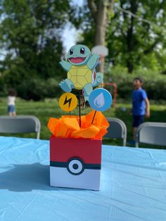 a pokemon centerpiece in a box on top of a blue table cloth with people standing behind it