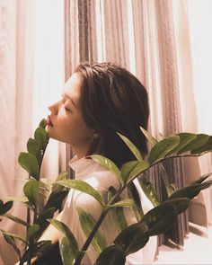 a woman standing next to a plant in front of a window