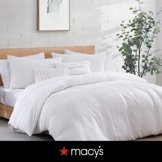 a bed with white sheets and pillows in a room next to a potted plant