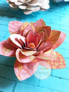 an origami flower sitting on top of a blue brick wall next to other paper flowers