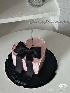 a pink and black heart shaped cake with a bow hanging from it's side