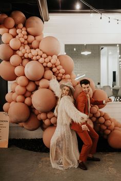 two people standing next to each other in front of a giant balloon wall with balloons on it