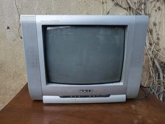 an old tv sitting on top of a wooden table next to a wall with vines