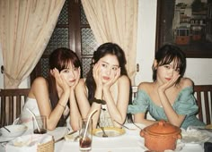 three young women sitting at a table with food and drinks in front of their faces