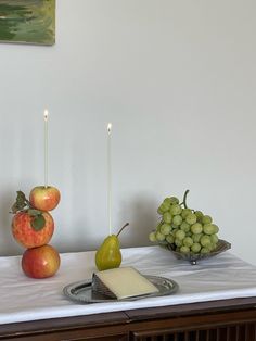 apples, grapes and cheese on a table with candles in the shape of pears