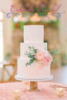 a white wedding cake with pink flowers and greenery sits on top of a table