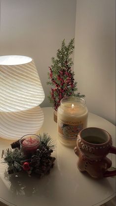 a table topped with a lit candle next to a vase filled with flowers and pine cones