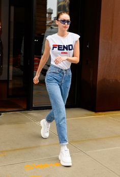 a woman in white shirt and jeans walking down the street with sunglasses on her face