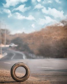 an old tire sitting on the side of a road in front of a cloudy sky