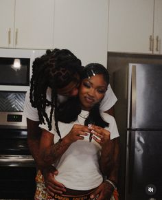 two people standing in a kitchen looking at a cell phone