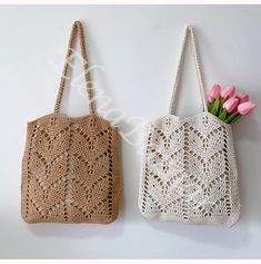 two crocheted bags hanging on the wall with pink flowers in front of them