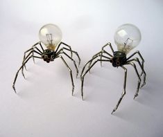 two light bulbs sitting next to each other on top of a white surface with a spider in it's legs