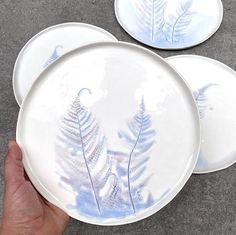 three white plates with blue designs on them are being held by a person's hand