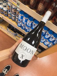 a person is holding a bottle of wine in front of shelves with sodas and beer cans