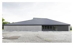 an empty parking lot in front of a building with a black roof and two windows